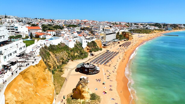 Un pueblo costero con una playa, un acantilado rocoso y un edificio con una estructura circular.