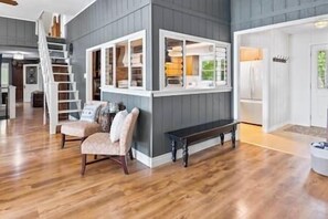 A spacious living area with a wooden floor, a bench, and a built-in shelving unit with various items. - Blue Heron Lakefront Cottage w/ Hot Tub (Kawartha Lakes)
