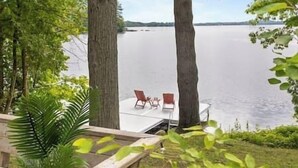 Um deck à beira do lago com duas cadeiras e uma mesa, rodeado por árvores.