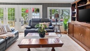 Uma sala de estar com uma mesa de centro de madeira, um sofá de couro preto e uma televisão em um armário de madeira.