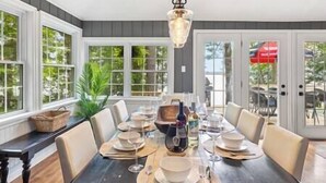 Uma sala de jantar com uma mesa grande posta para seis pessoas, rodeada por cadeiras, e um lustre pendurado acima.