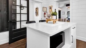 Una cocina moderna con armarios blancos, una puerta negra y una isla de madera con una planta.