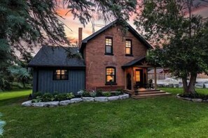 Une maison à deux étages, avec un toit sombre, un porche à l’avant et une pelouse bien entretenue.