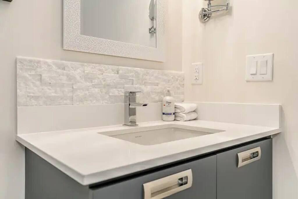 A modern bathroom with a white sink, grey cabinets, and a decorative mirror.