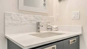 A modern bathroom with a white sink, grey cabinets, and a decorative mirror.