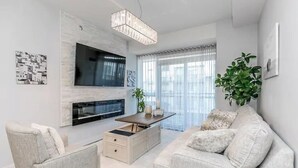 Un salon moderne avec un téléviseur à écran plat fixé au mur, une table basse en bois, un canapé beige et une plante en pot.