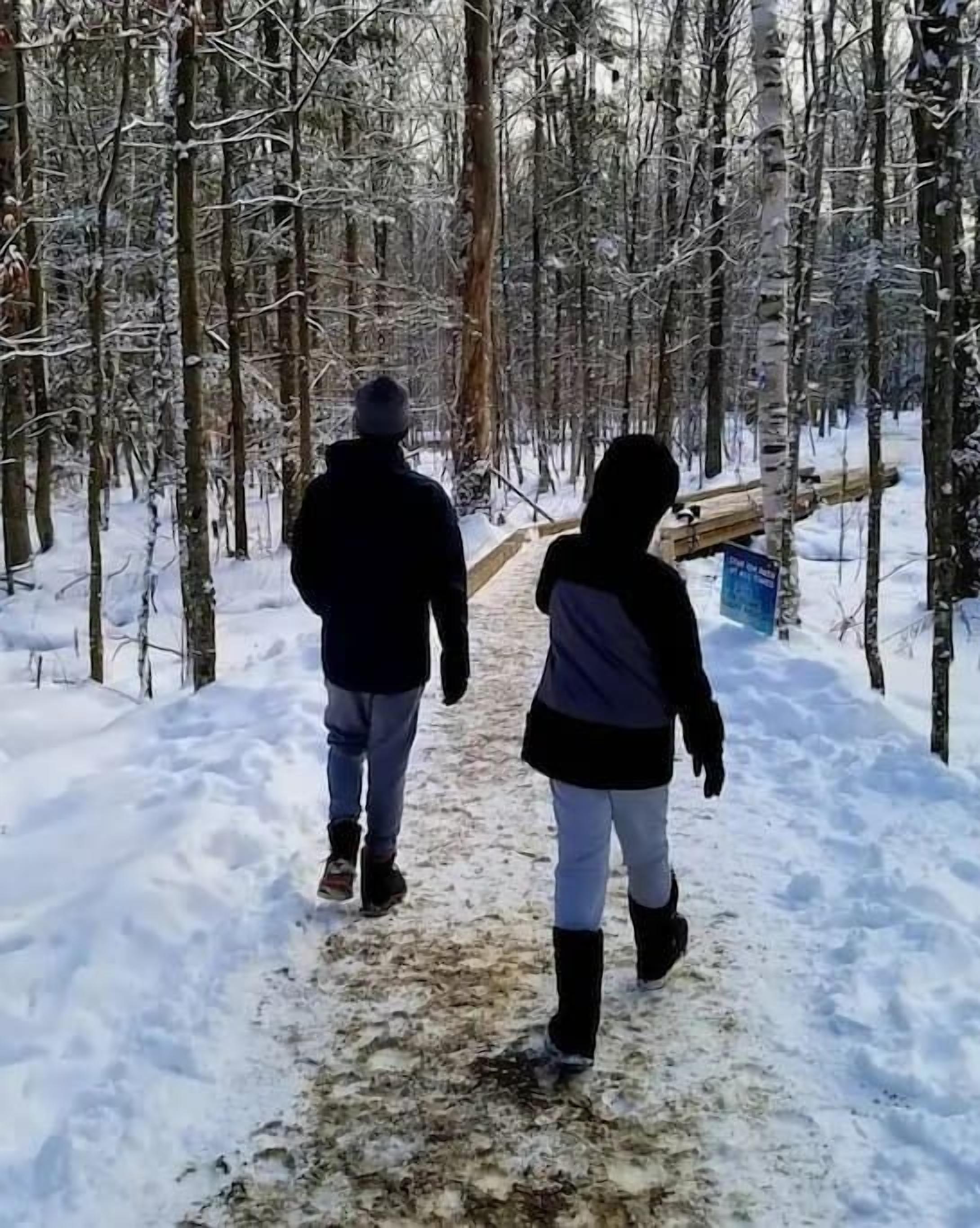 Un sentier enneigé à travers une forêt, où l’on voit deux personnes qui marchent.