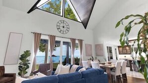 Ein geräumiges Wohnzimmer mit großem Fenster, einer Wanduhr und einem Essbereich mit Stühlen und Tisch.