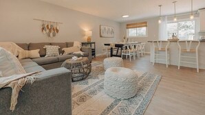 En moderne stue med en grå sofa, et sofabord og et spiseområde med hvide stole.