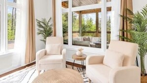 A room with two beige armchairs, a round coffee table, and a view of a deck with outdoor furniture. - Lake of Bays Beach Resort w Hot Tub, Sauna & Games (Lake of Bays)