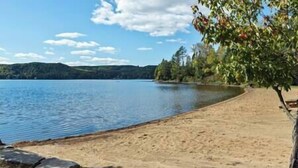 A sandy beach with calm water, a clear sky, and trees in the background. - Lake of Bays Beach Resort w Hot Tub, Sauna & Games (Lake of Bays)