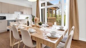 A modern kitchen with white cabinets, a dining table set for four, and a large window with curtains. - Lake of Bays Beach Resort w Hot Tub, Sauna & Games (Lake of Bays)