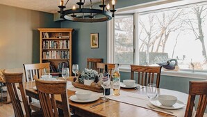 Un comedor con una mesa de madera dispuesta para cuatro personas, rodeada de sillas de madera. Sobre la mesa, un candelabro y a la izquierda, una estantería.