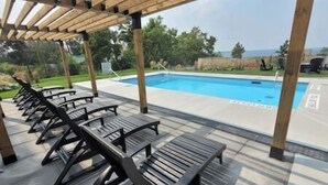 Un espacio al aire libre techado con piscina, sillas de descanso y vistas del paisaje.