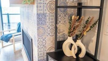 A room with patterned wallpaper, a vase with dried plants, and a chair with a blue cushion.