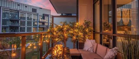 Un balcón con sofá, una mesa con chimenea y luces colgantes.