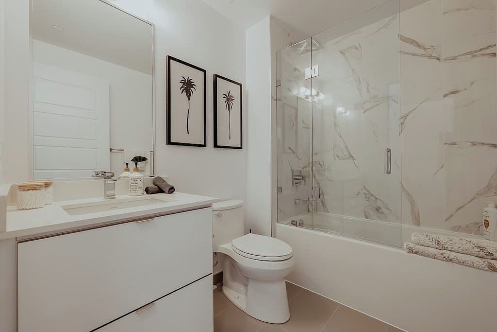 A modern bathroom with a white vanity, a toilet, and a glass-enclosed shower.