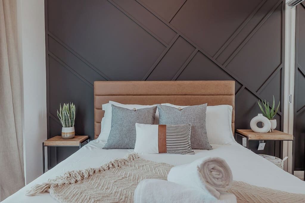 A modern bedroom with a large bed, a wooden headboard, and two bedside tables with plants.