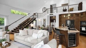 Amplia sala de estar con una escalera que sube a un altillo, una cocina con una isla grande y una zona de estar acogedora.