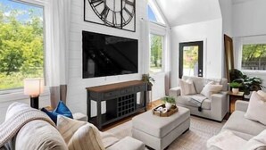 Un salón amplio con chimenea, asientos cómodos y ventanas grandes que ofrecen vistas al exterior.