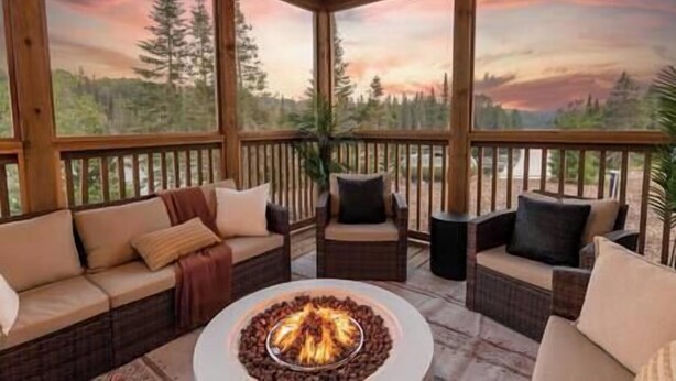 A covered outdoor seating area with a fire pit, wooden furniture, and a scenic view of trees and mountains. - The Algonquin Lakehouse w Hot Tub, Games, Fire Pit (Huntsville)