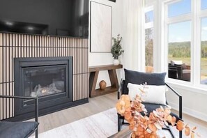 Ein modernes Wohnzimmer mit Kamin, einer Couch und Blick ins Freie.