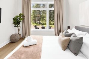 A bedroom with a large window, a bed with grey and white bedding, a plant, and a round cushion on the floor. - Hot Tub & Wood Burning Sauna - Muskoka Birch House (Lake of Bays)