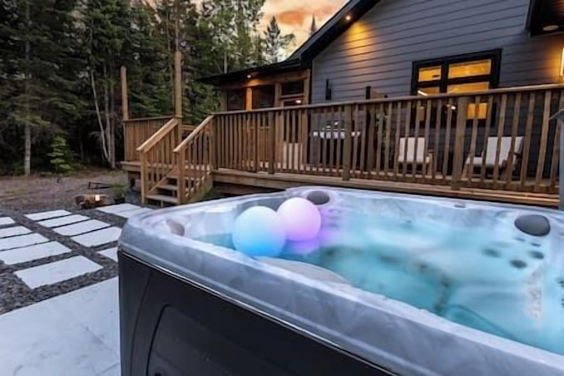 Ett bubbelbad med tre färgglada bollar, ett trädäck och ett hus i bakgrunden.