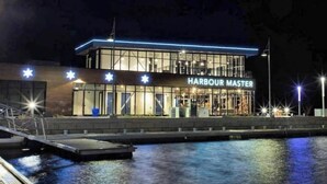 A waterfront building named 'Harbour Master' with a dock and a calm water body in the foreground.