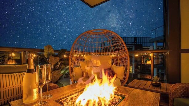 A night scene with a fire feature, a bottle of champagne, and a starry sky visible through a glass enclosure.