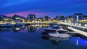 A marina with boats docked, waterfront buildings, and a calm evening sky.