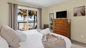 Ein Schlafzimmer mit Bett, Kommode, Fernseher und Blick auf den Strand.
