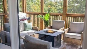 A covered outdoor seating area with wicker furniture and a central fire feature. - Northern Lights Muskoka w/ Hot Tub & Pool Table (Muskoka District Municipality)