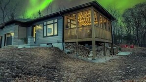 A house with a wooden deck and large windows, surrounded by trees. - Northern Lights Muskoka w/ Hot Tub & Pool Table (Muskoka District Municipality)