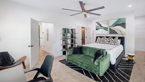 Une chambre moderne avec un lit, un canapé vert, un bureau et un ventilateur de plafond.