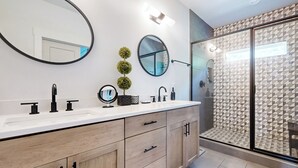 Une salle de bain moderne avec un grand miroir, deux petits miroirs ronds, un lavabo avec des robinets noirs et une douche aux carreaux décorés.