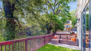 Un balcon doté d’une balustrade en bois, une zone herbeuse et un espace aménagé avec des coussins pour s’asseoir.