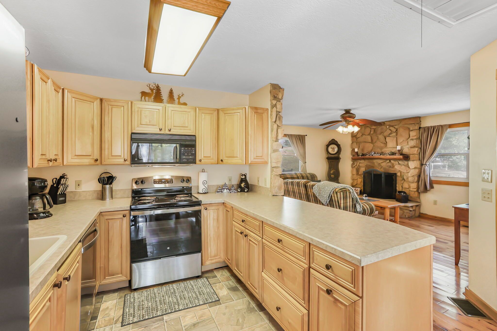 A kitchen with wooden cabinets, a stove, microwave, and a stone fireplace.