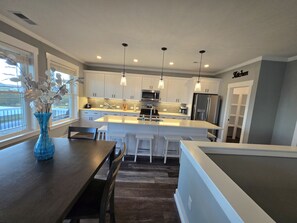 A modern kitchen with white cabinets, stainless steel appliances, and pendant lighting. - Spacious Beach Home for Large Groups • Sleeps 14 • Walk to Access (Oak Island)