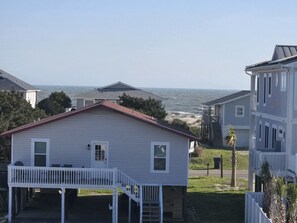A coastal house with a balcony, a view of the ocean, and a neighboring building. - Spacious Beach Home for Large Groups • Sleeps 14 • Walk to Access (Oak Island)