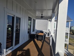 A covered porch with a table and chairs, large sliding glass doors, and a ceiling fan. - Spacious Beach Home for Large Groups • Sleeps 14 • Walk to Access (Oak Island)
