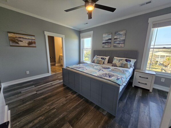 A bedroom with a large bed, a ceiling fan, and a window with a view. - Spacious Beach Home for Large Groups • Sleeps 14 • Walk to Access (Oak Island)