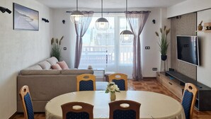 A dining area with a round table, four chairs, a sofa, and a television on the wall. - Amazing apartment in Omis (Omis)