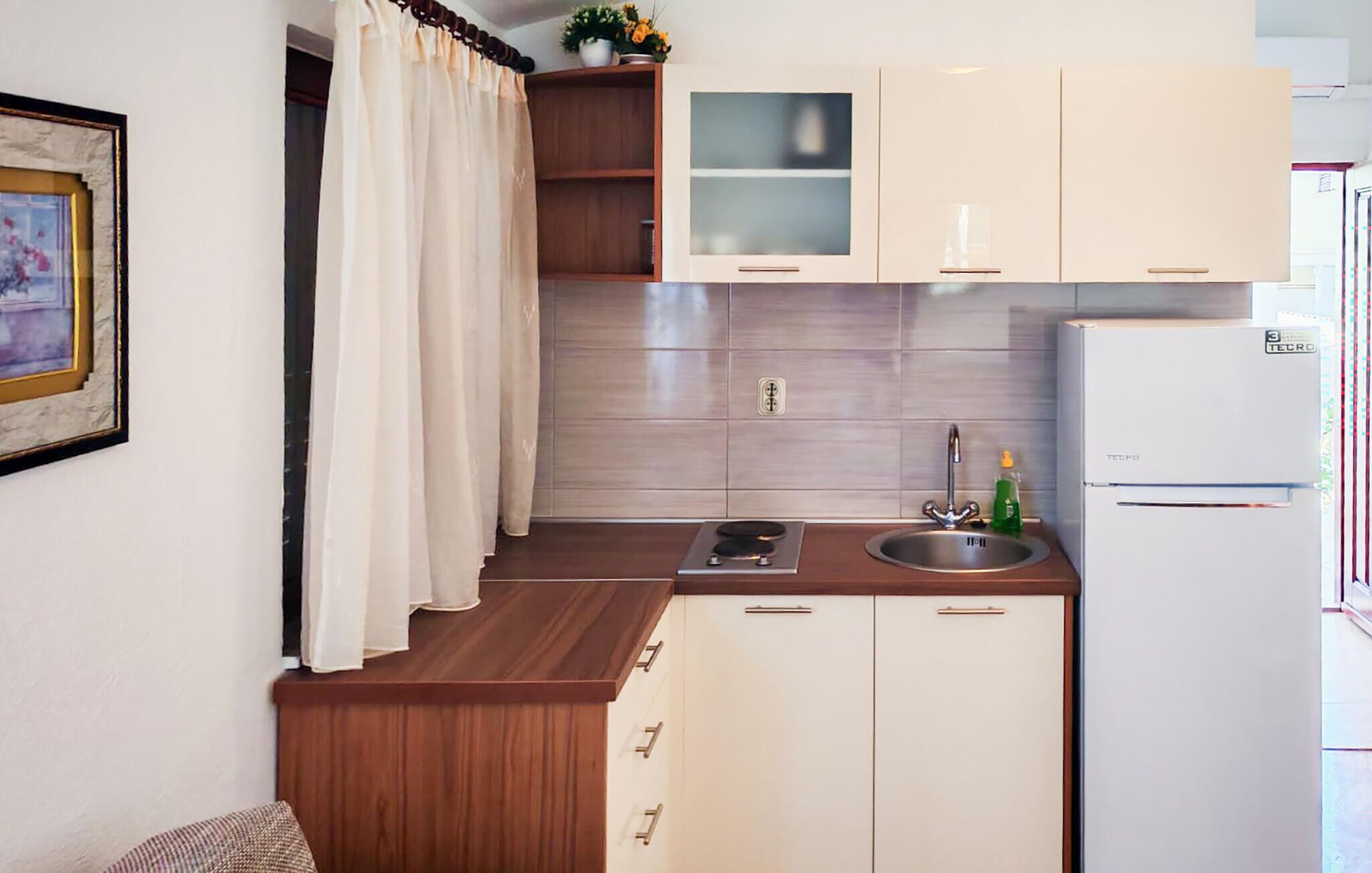 A compact kitchen with wooden cabinets, a white refrigerator, a sink with a faucet, and a small countertop with a stove.