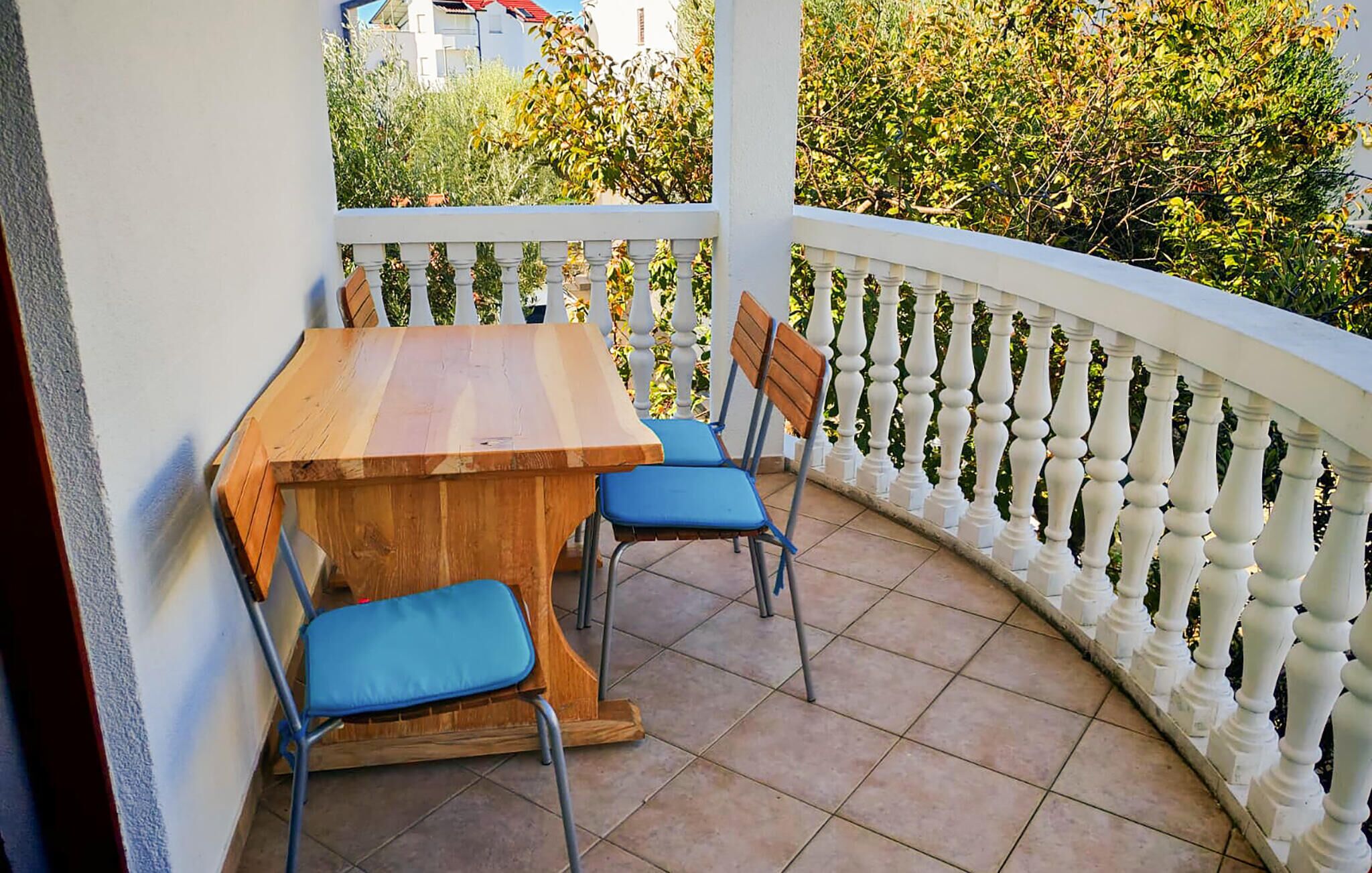 A covered outdoor patio with a wooden table and two blue chairs, surrounded by a white balustrade.