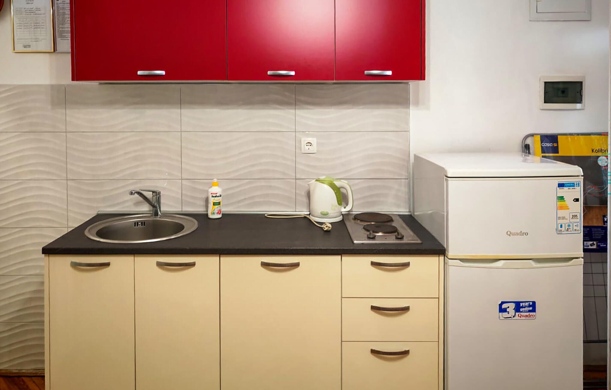A kitchen with a sink, a kettle, a refrigerator, and a cabinet with drawers.