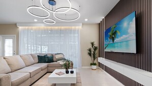 Uma sala de estar moderna com um sofá seccional, uma mesa de centro branca e uma pintura grande com uma cena de praia.