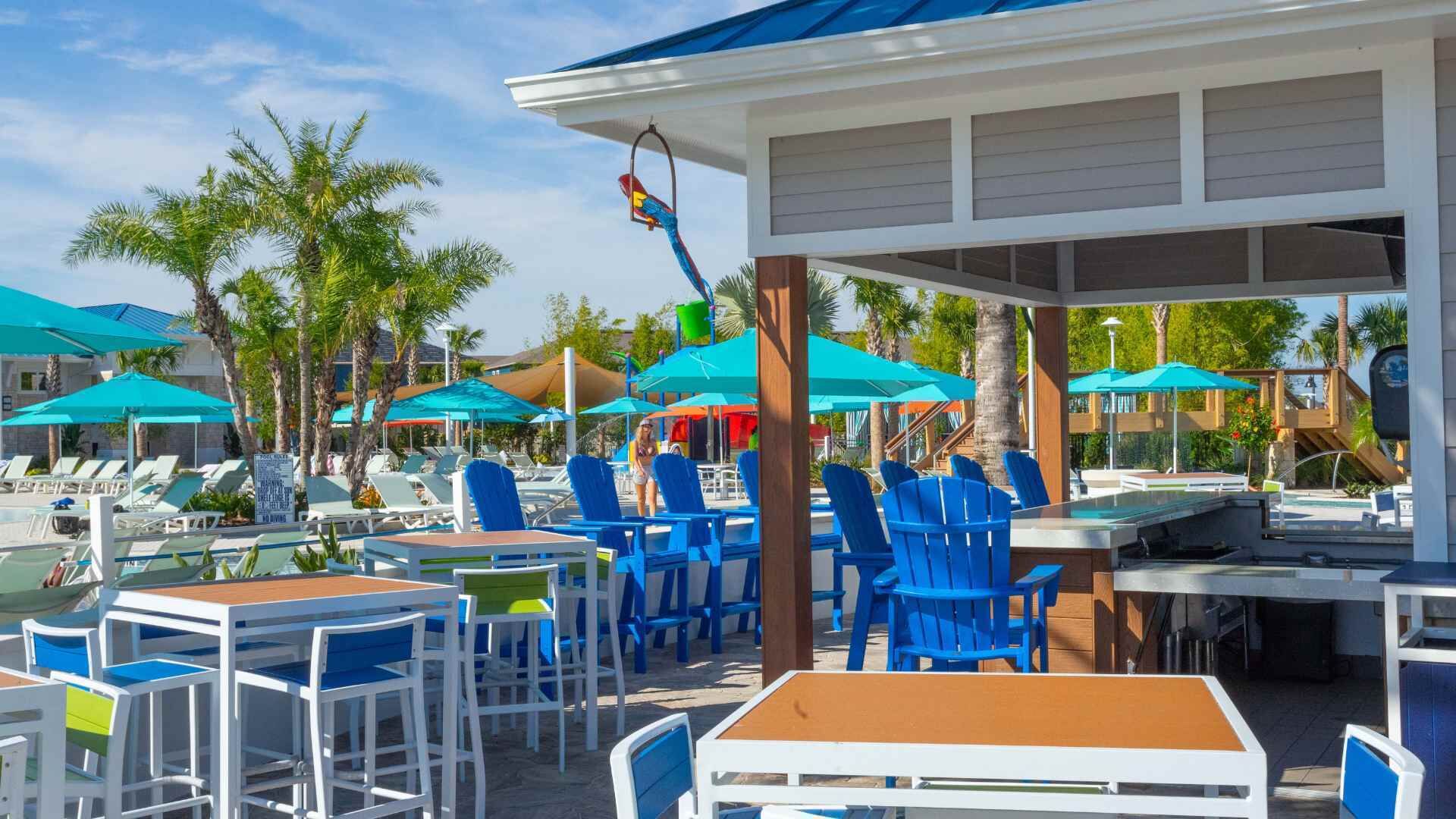 A beachside restaurant with outdoor seating, palm trees, and umbrellas.
