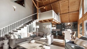En rummelig opholdsstue med et moderne sofasæt, et spisebord og en trappe til et øvre niveau.