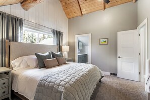 Ein Schlafzimmer mit einem großen Bett, einem Nachttisch, einer Lampe, einer Tür und einem Fenster mit Vorhängen.